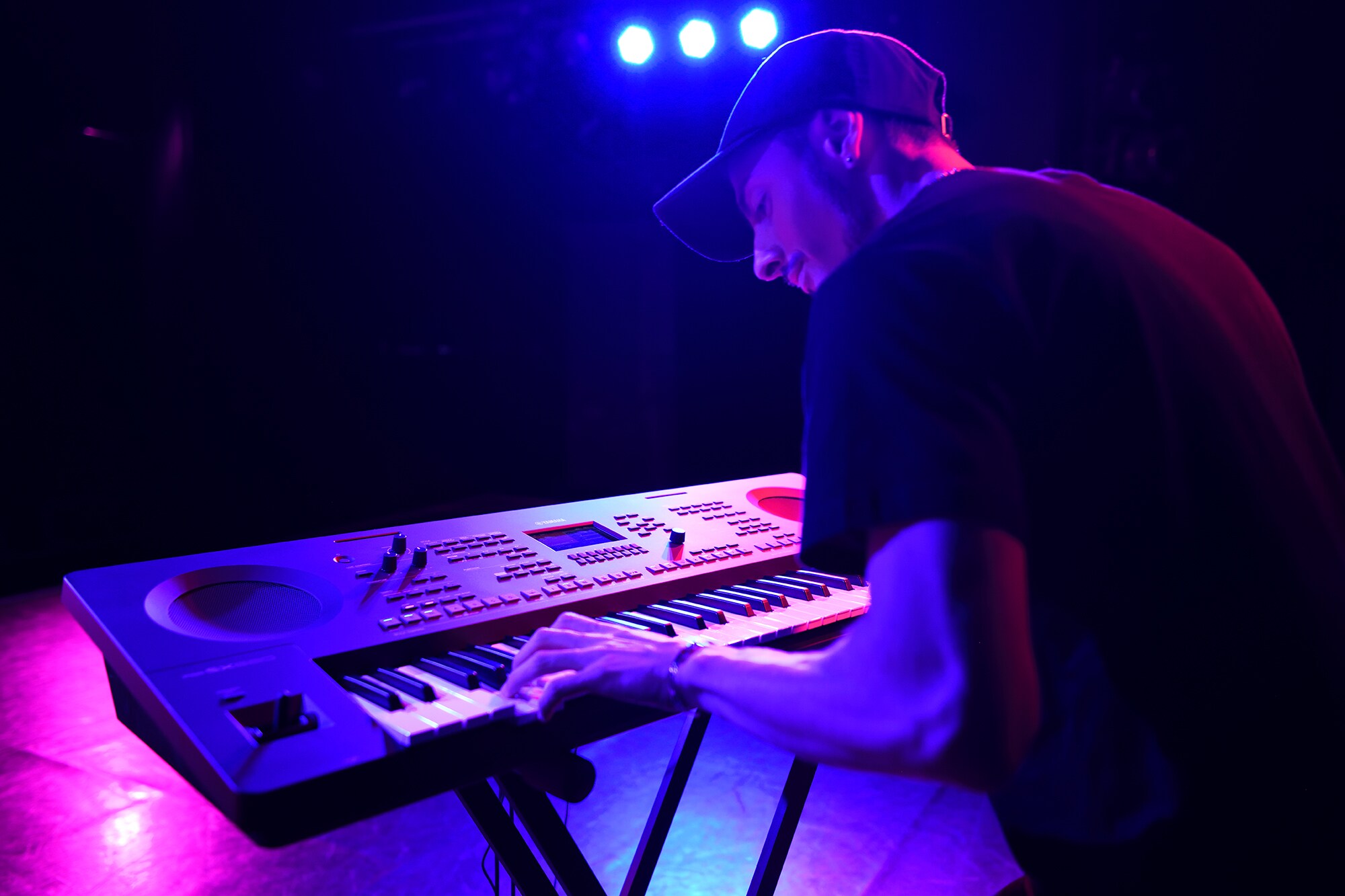 Uma pessoa tocando num Arranjador Workstation Yamaha em um suporte sob iluminação de palco