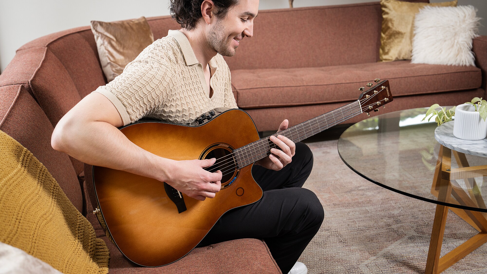 Um homem sentado em um sofá na sala de estar tocando um violão TAG3 C