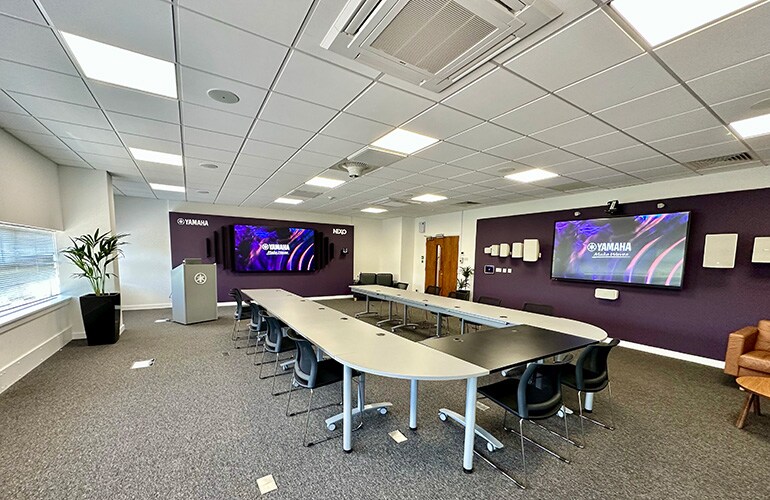 Centro de treinamento de Milton Keynes, com mesas, cadeiras, tela de exibição e equipamentos de áudio.