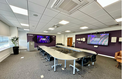 Centro de treinamento de Milton Keynes, com mesas, cadeiras, tela de exibição e equipamentos de áudio.
