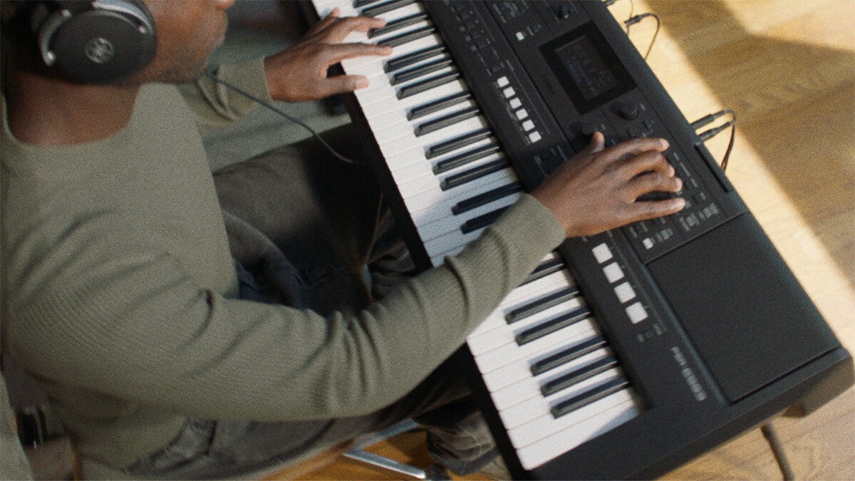 Uma pessoa tocando o Teclado Portátil Yamaha PSR-E483 com fones de ouvido