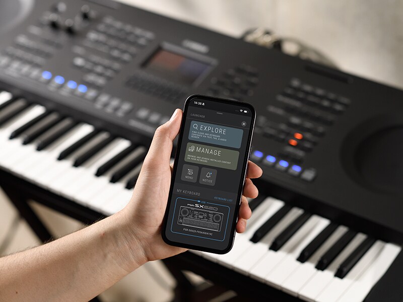 PSR-SX920 e uma mão segurando um smartphone com a tela de um player de música.