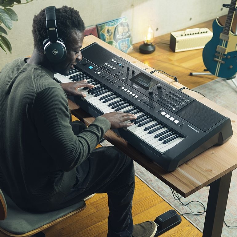 Uma pessoa tocando o Teclado Portátil Yamaha PSR-E483 com fones de ouvido