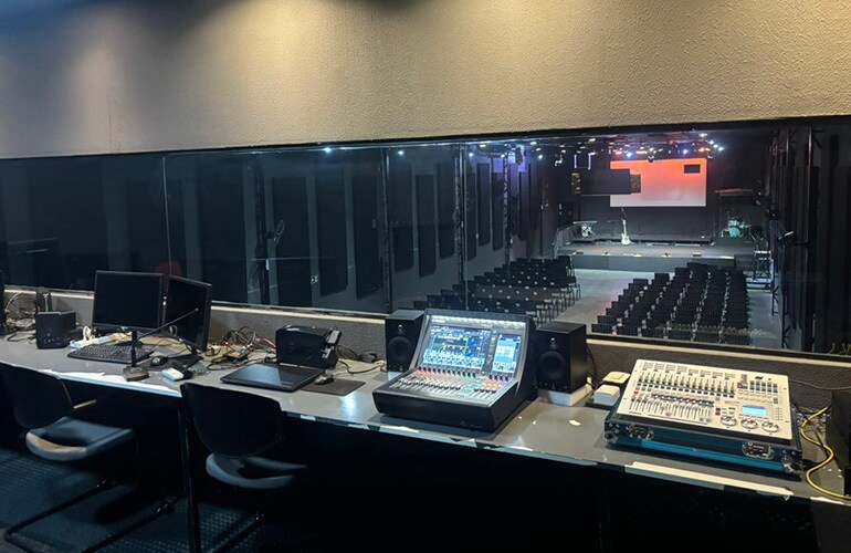 Sala de controle do centro de treinamento de São Paulo, com consoles de mixagem digital, telas e racks de equipamentos de áudio.