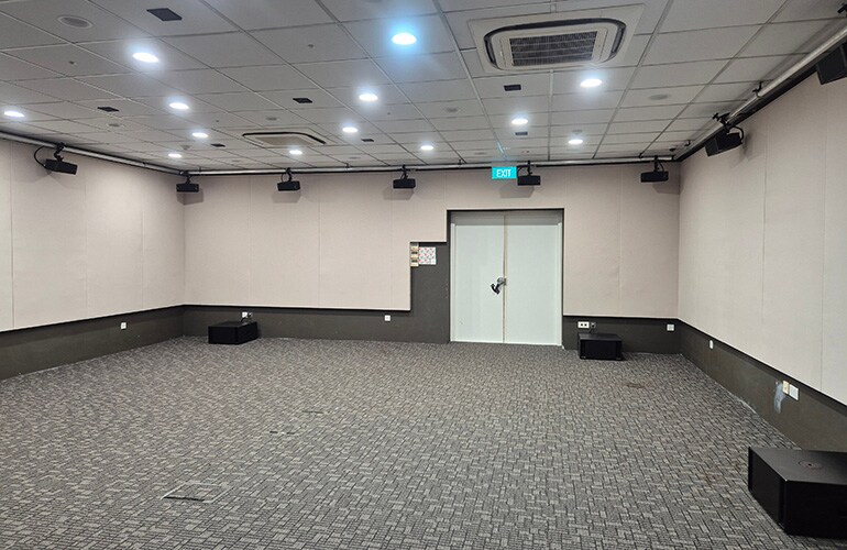 Sala do centro de treinamento de Singapura, com assentos, tela de apresentação e equipamentos de áudio.