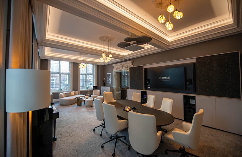 Sala de reunião do centro de treinamento de Londres, com mesas, assentos e tela de exibição.