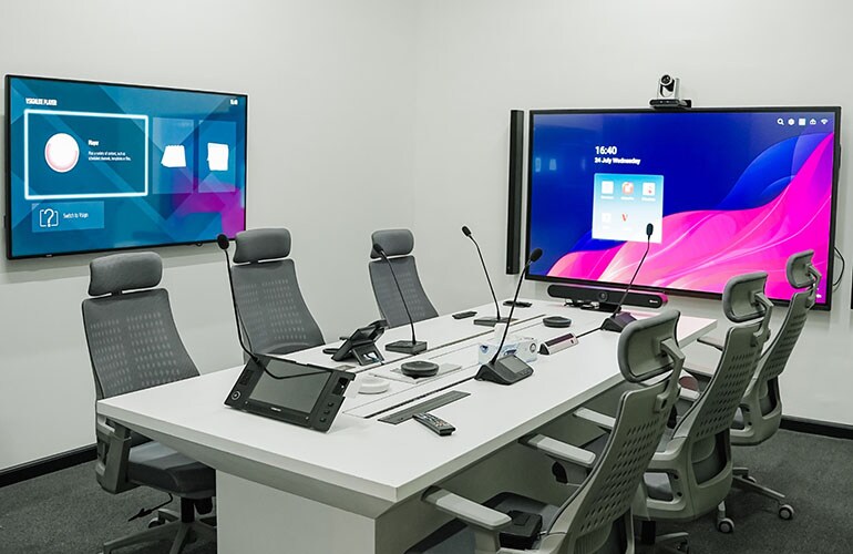 Sala de reunião do centro de treinamento de Dubai, com mesa de conferência, telas de vídeo e equipamentos de apresentação.