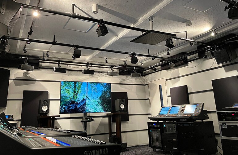Centro de treinamento de Yokohama, com uma tela grande, consoles de mixagem digital, caixas acústicas e equipamentos de áudio.