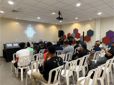 Centro de treinamento de Santo Domingo, com participantes sentados em uma sessão de treinamento de áudio em formato sala de aula.